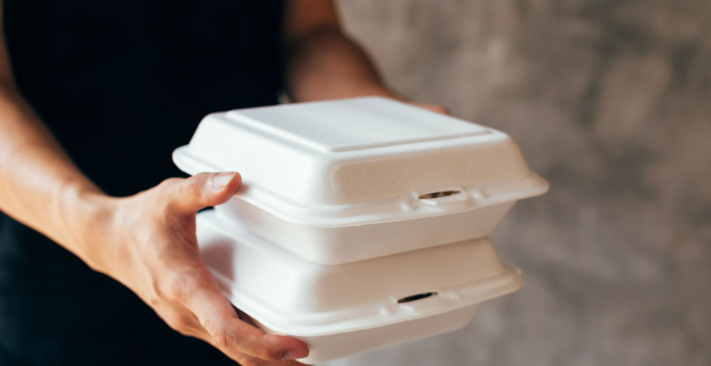 Livreur professionnel transportant cartons de plateaux-repas sur chariot dans couloir d'immeuble de bureaux parisien moderne, en mouvement naturel